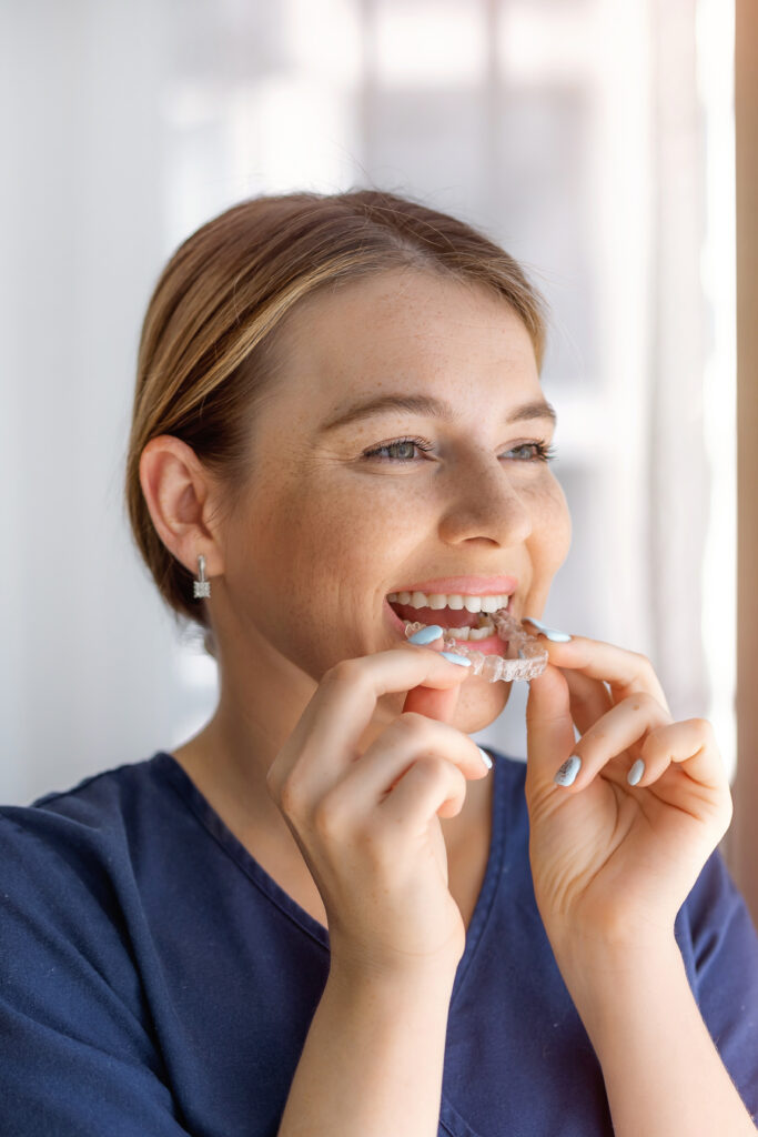 Woman smiling putting in Invisalign aligners, Russell Orthodontics in Grayson and Athens